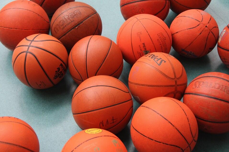 Ansammlung von orangefarbenen Basketballen auf einer grünen Unterlage, verschiedene Marken und Größen sichtbar.