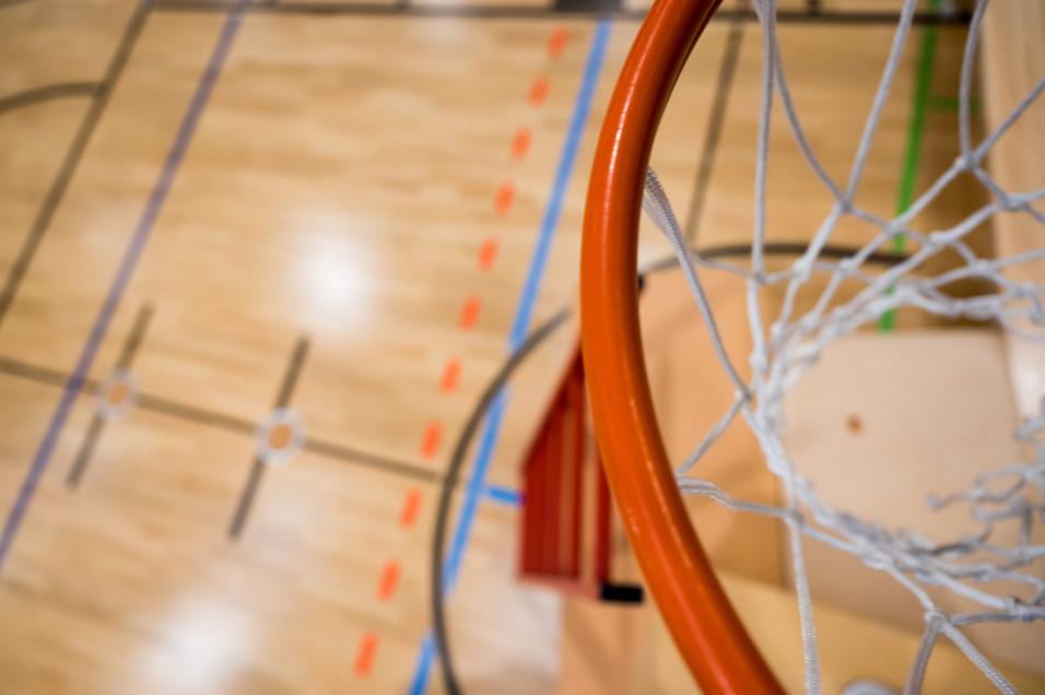 Nahaufnahme eines Basketballkorbs mit Netz über einem aufgezeichneten Basketballfeld aus Holz.