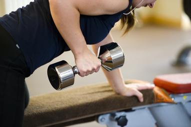 Frau macht eine Bizepsübung mit einer Hantel, während sie auf einer Trainingsbank lehnt.