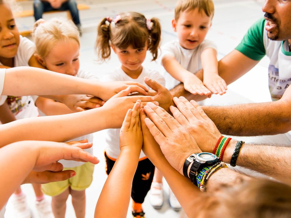 Kinder und Erwachsene legen ihre Hände in einem Kreis zusammen, symbolisieren Zusammenarbeit und Gemeinschaft.