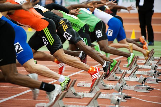 Start einer Sprintveranstaltung mit mehreren Athleten in Blockstartposition auf einer Laufbahn.