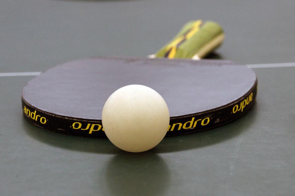 Nahaufnahme eines Tischtennisschlägers mit weißem Ball auf einer grünen Tischtennisplatte.